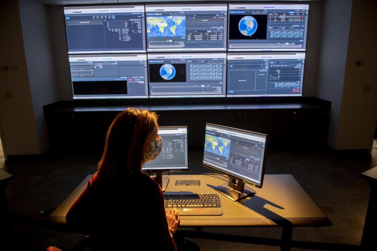 Employee of Raytheon works at a computer in front of large screen.