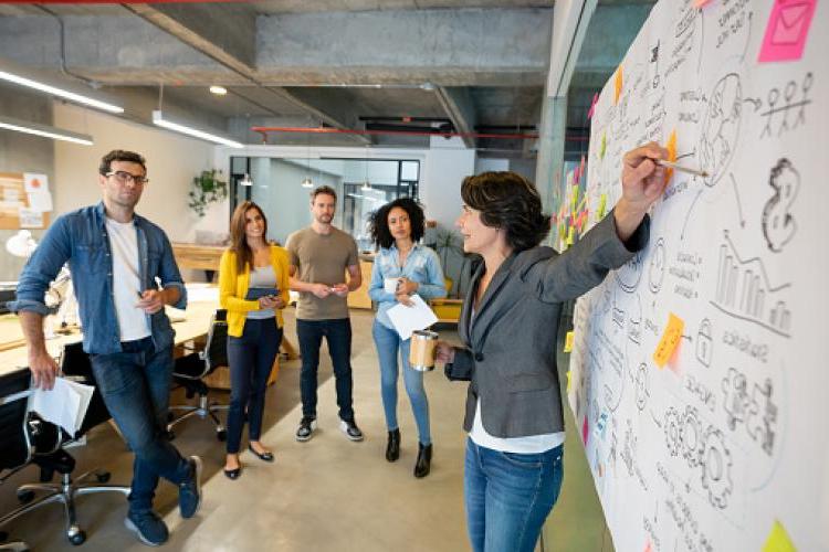 woman pointing at whiteboard presenting to a group of people