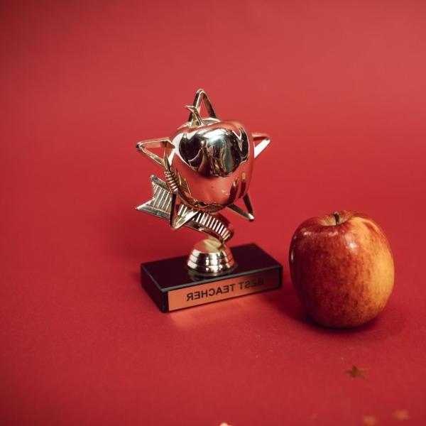 an award trophy for best teacher on a red table next to a red apple