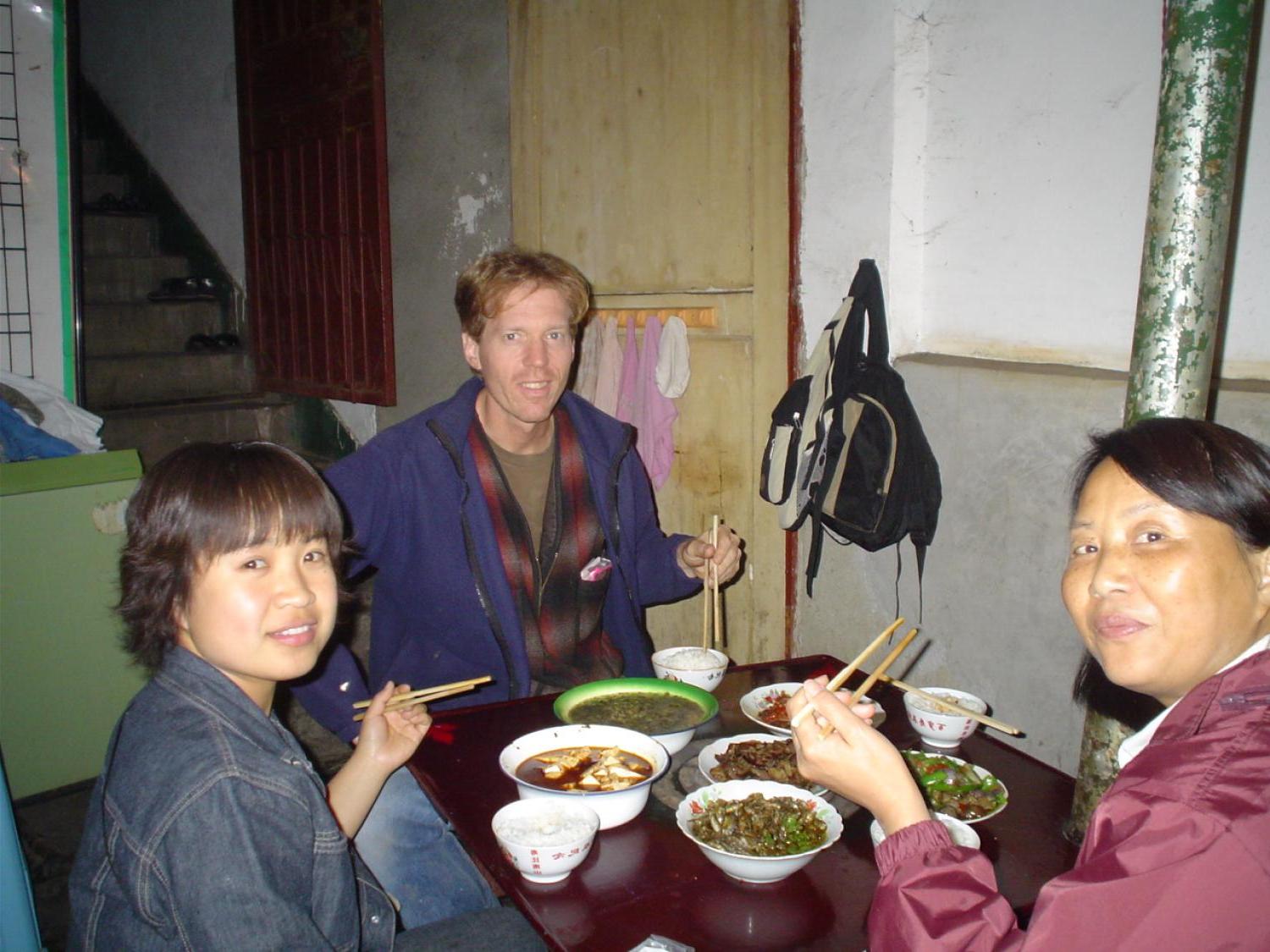 Caucasian man with chopsticks eating dinner with 2 Chinese women