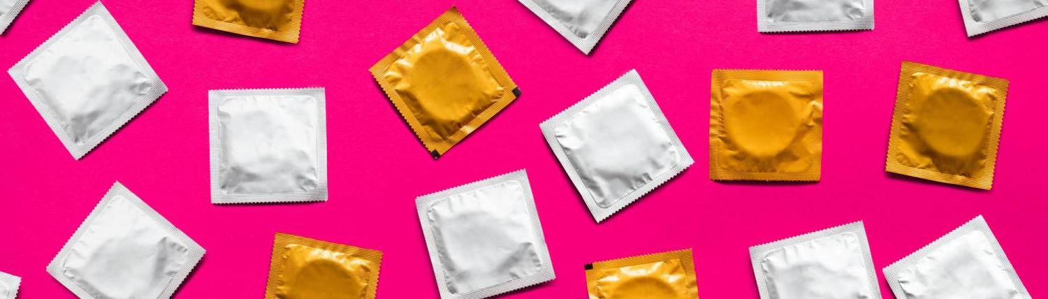 Photo of different colored condom packages on a hot pink background.