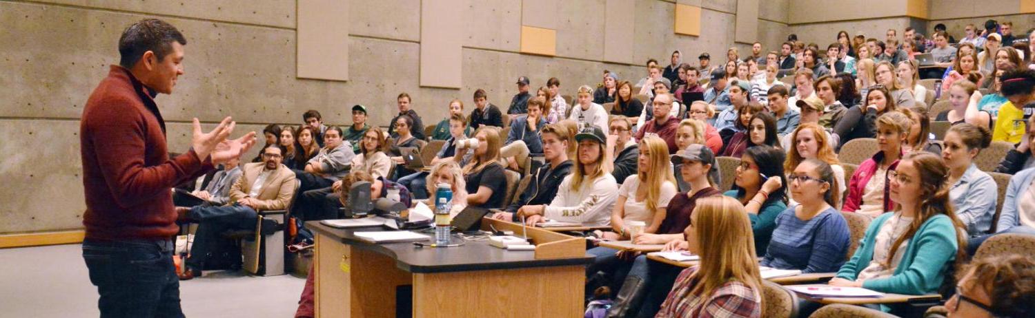 Photo of a faculty member giving a lecture in front of an auditorium full of students.