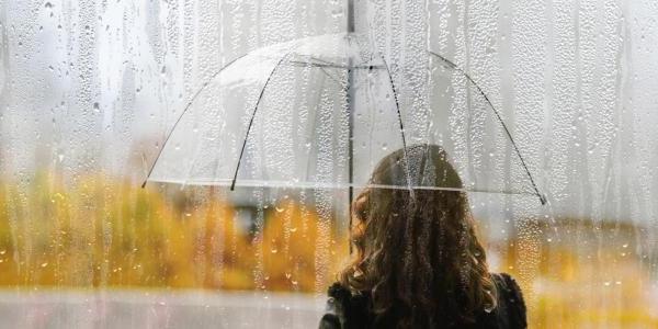 穿着黄色雨衣的女人站在雨中，手里拿着一把透明的雨伞.