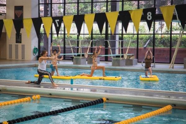 instructor guiding students in paddleboard yoga class at indoor pool