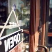 women looking at 'open' sign through window of business 